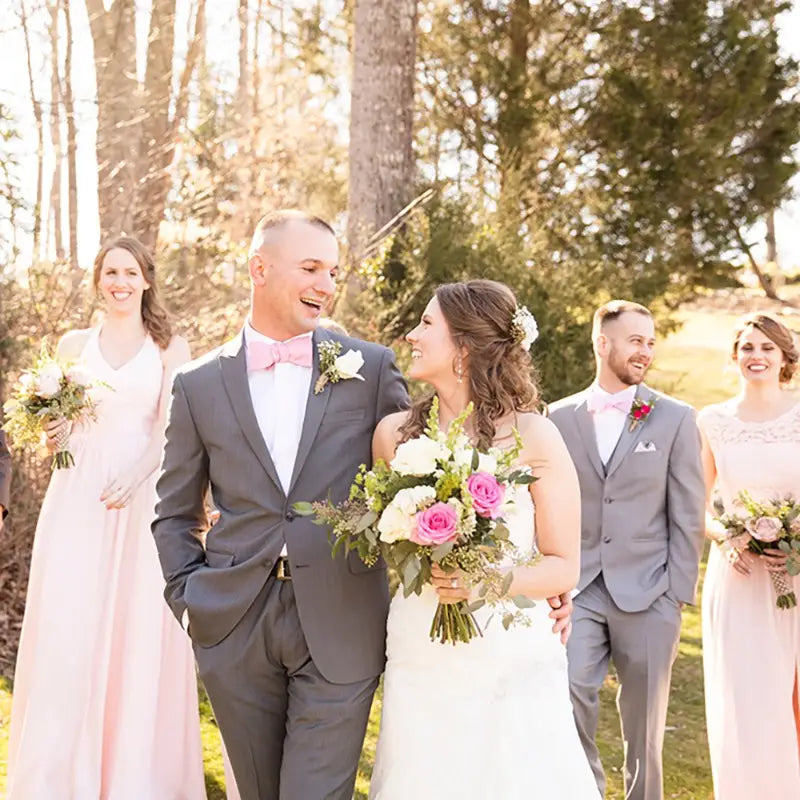 新婦はピンクのバラとグリーンをあしらったフローラルのブライダルブーケが特徴のラインストーンの結婚指輪リングピローを手に持ち、繊細なレース仕立ての白いウェディングガウンを身に着けています。