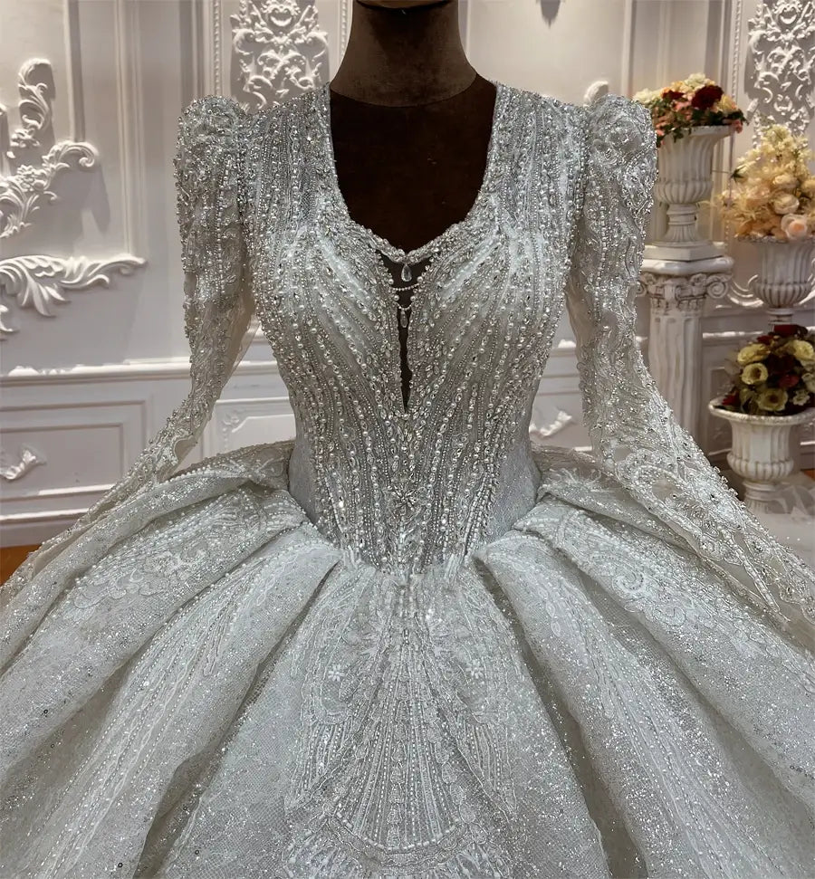 Robe de mariée sur mesure à manches longues en dentelle et jupe en forme de cloche, argenté scintillant, avec de longues manches bouffantes, une jupe volumineuse, et des applications complexes de perles et de sequins.