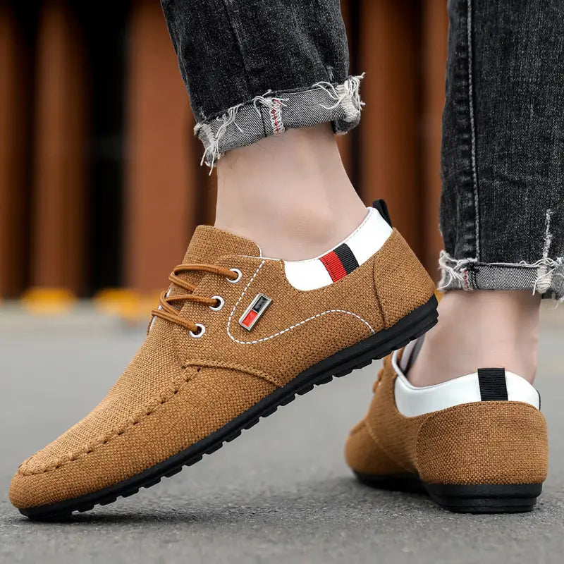 Men’s casual canvas sneakers lightweight daily footwear in tan with lace-up design white and black accents and a small red and black logo patch on the side.