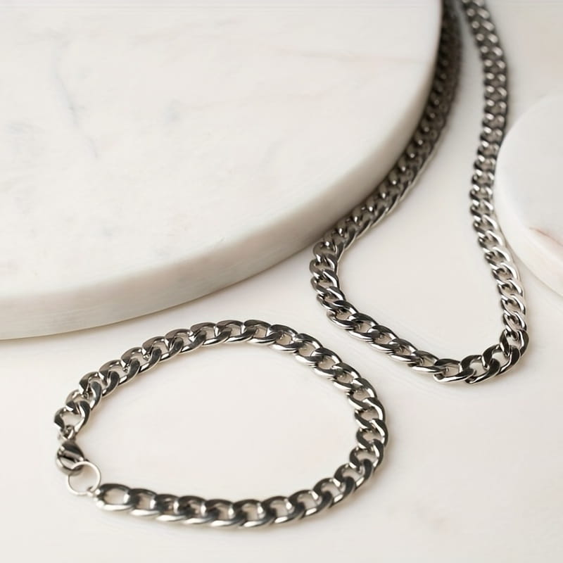 Ein elegantes Set aus dunkelfarbener silberner Cuban-Link-Kettenhalskette und passendem Armband für Herren mit polierter Metalloberfläche.