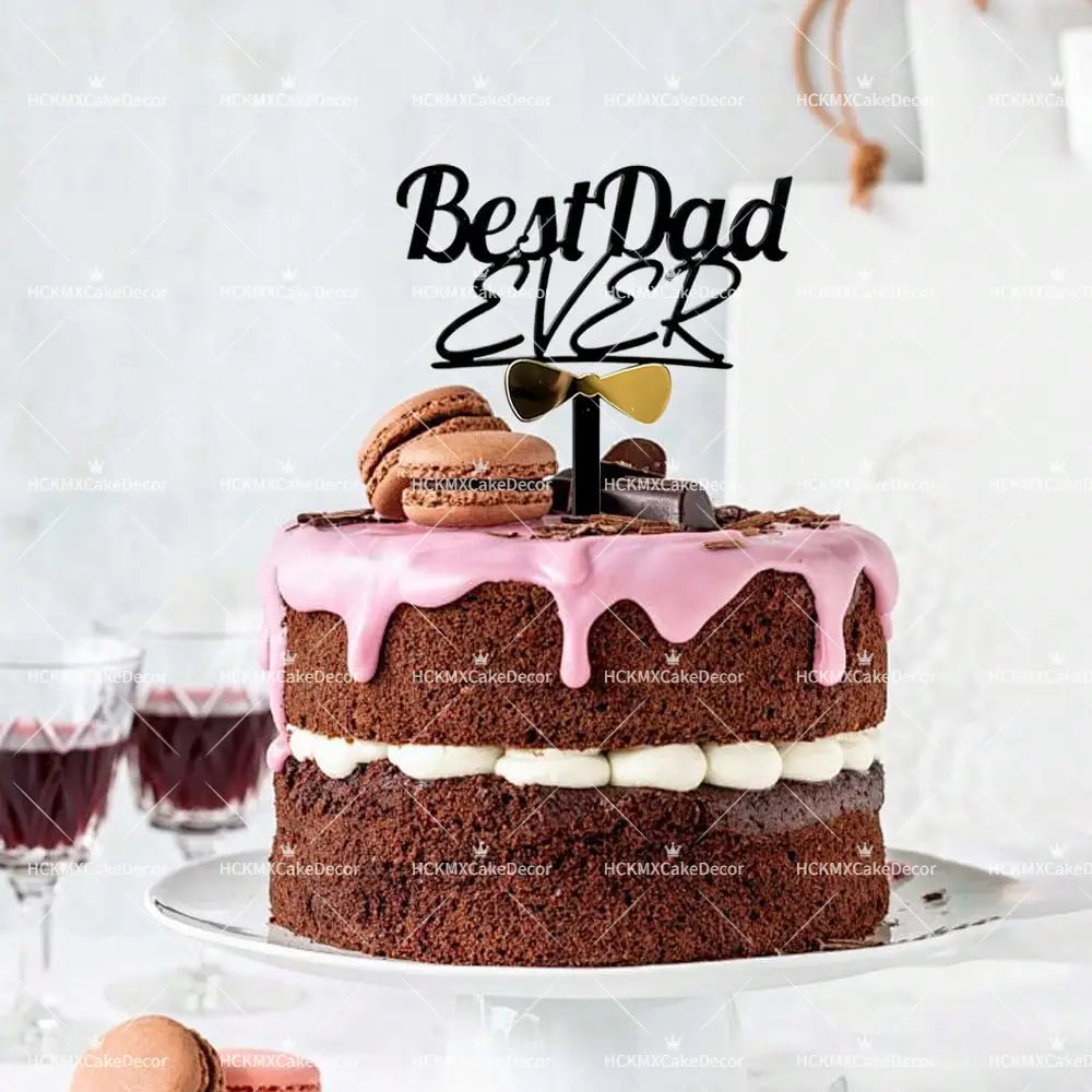 A chocolate cake with pink icing drizzle and white cream layers topped with a black and gold best dad ever acrylic cake topper featuring a bow tie for fathers day.