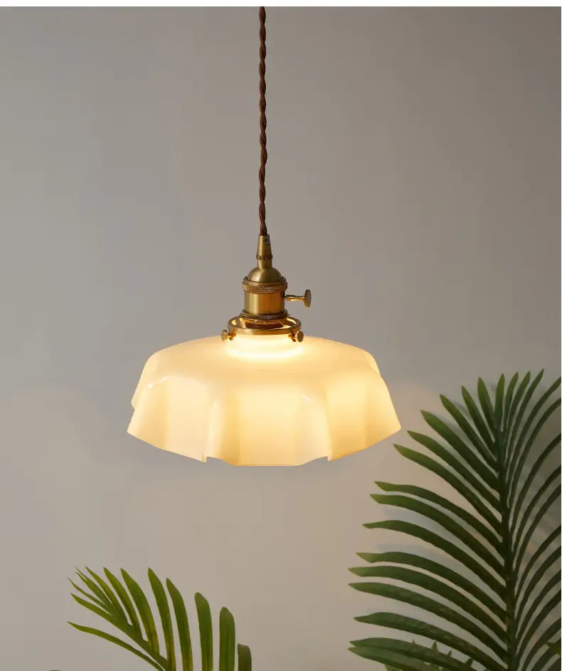 Un luminaire suspendu à jupe florale en verre crème chaud avec une tête de lampe en cuivre et un cordon brun torsadé, vu depuis un angle avant.