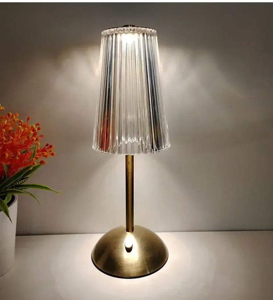 Eine elegante wiederaufladbare Tischlampe mit polierter Messingbasis und einem klaren, vertikal gerippten Glasschirm als elegante Lichtquelle.