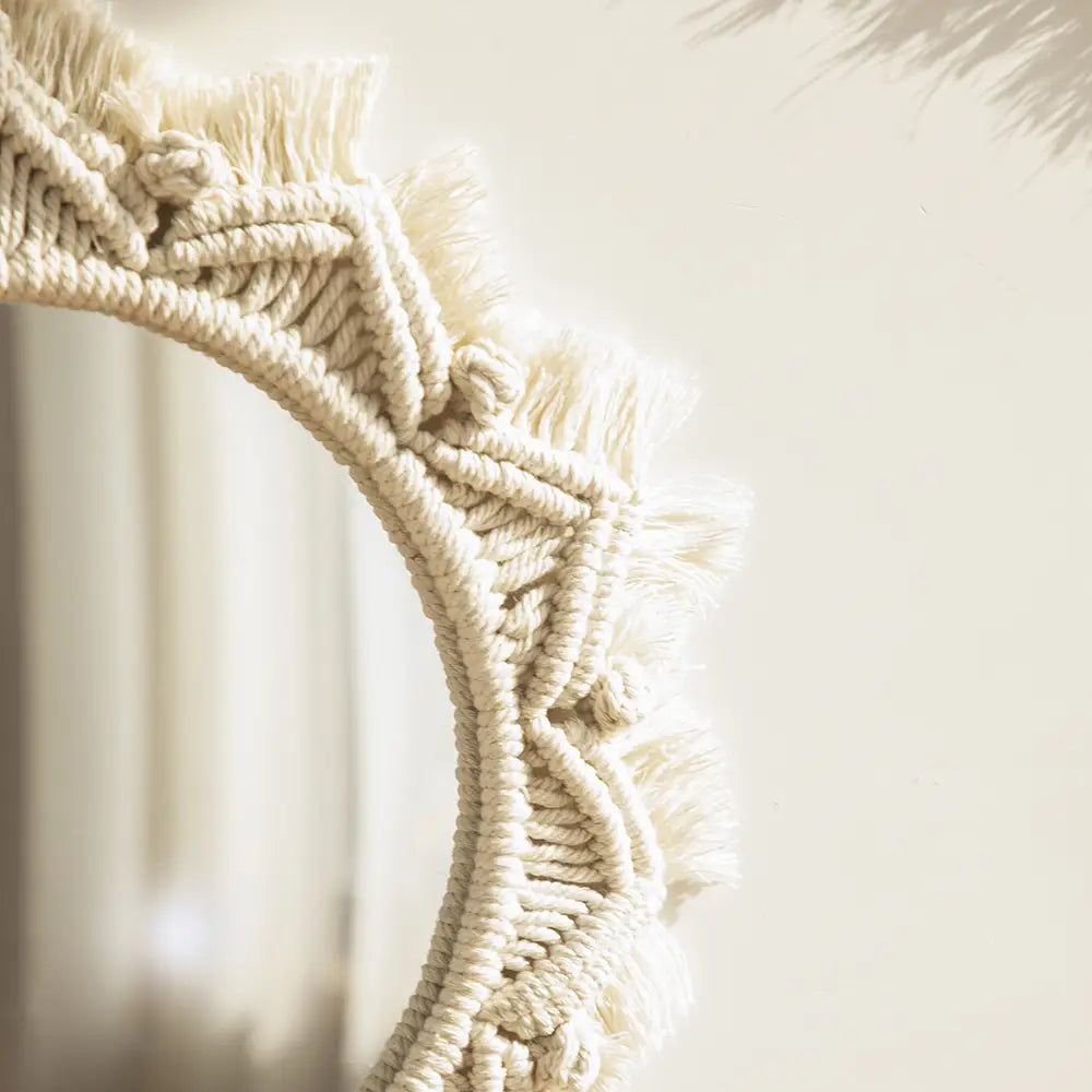 Cream-colored macrame wall mirror with intricate woven patterns and soft fringe detailing for living room home decor.