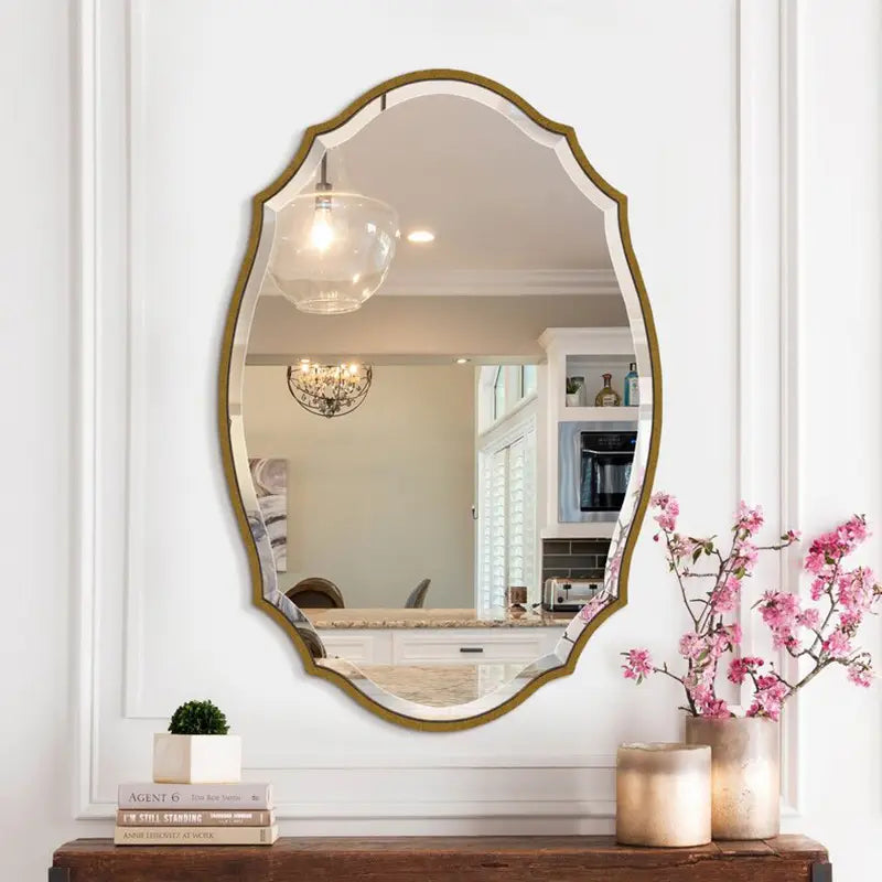 Un miroir de salle de bains ovale doré ornemental élégant, de style à cadre décoratif, est suspendu sur un mur blanc au-dessus d’une table console en bois.