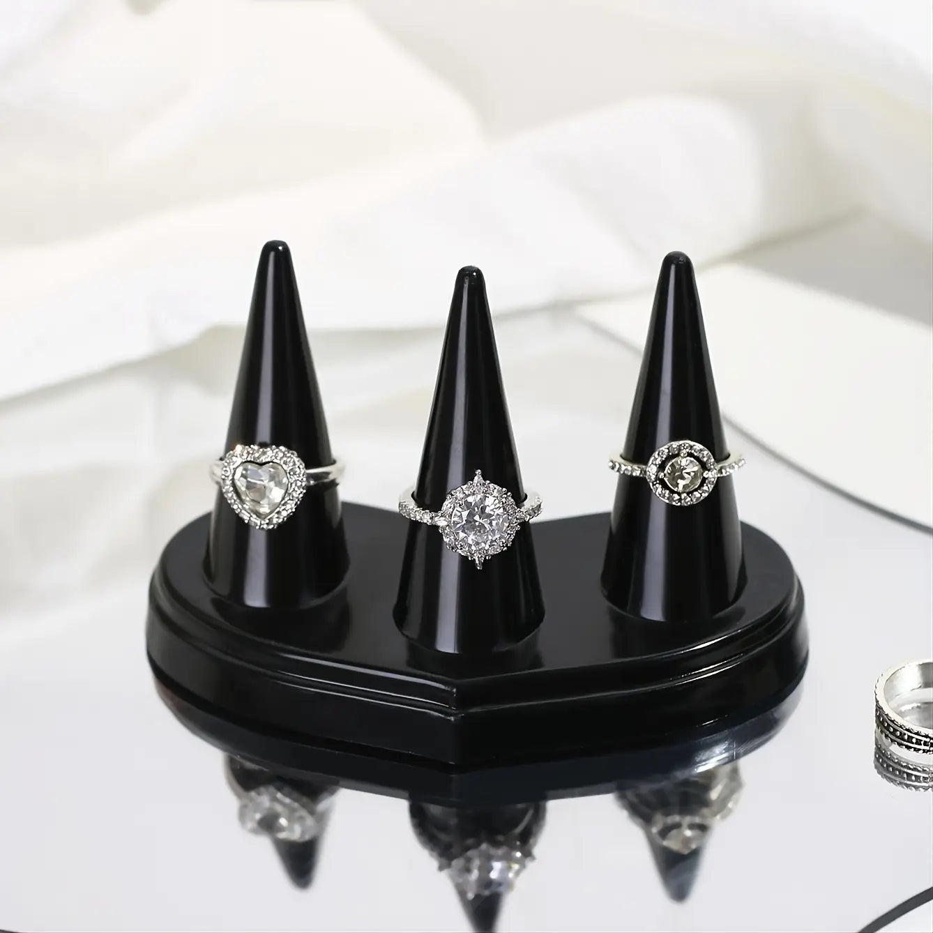 Support d’exposition en plastique noir conique pour bagues, avec trois logements pour présenter des bagues serties de diamants.