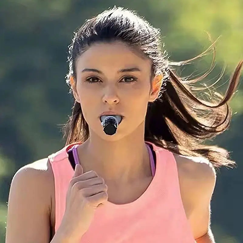 A black plastic whistle held in a womans mouth used as a lung capacity training device and respiratory fitness tool.