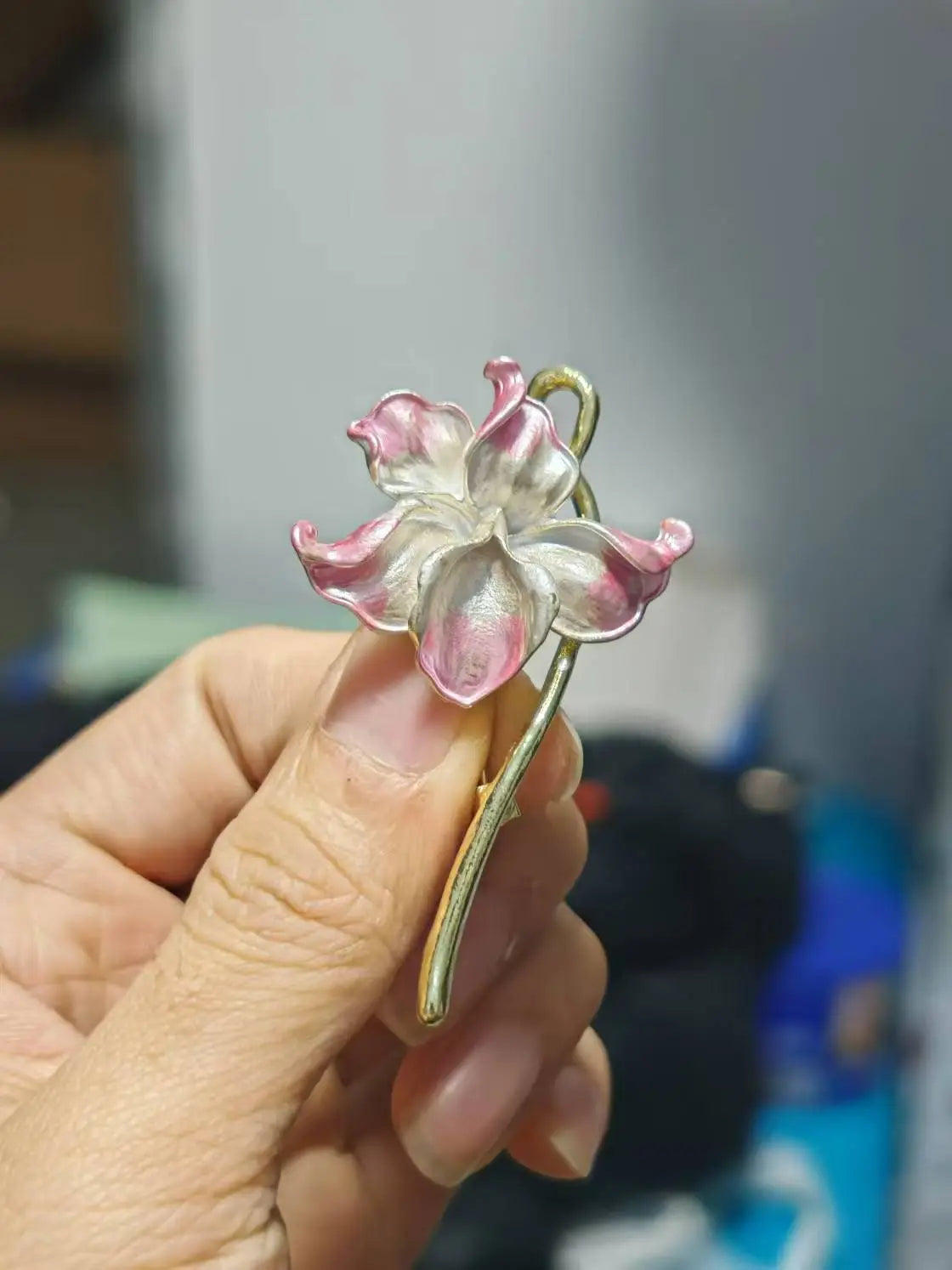 Une délicate broche-épingle émaillée en forme de fleur de lotus rose et blanche, avec une tige mince à ton doré.