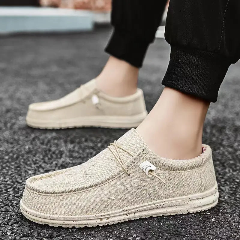 Chaussures décontractées de type mocassins à enfiler en toile pour hommes, confectionnées en lin beige, avec une semelle en caoutchouc à motifs d’aspérités et des lacets blancs pour un usage décontracté.