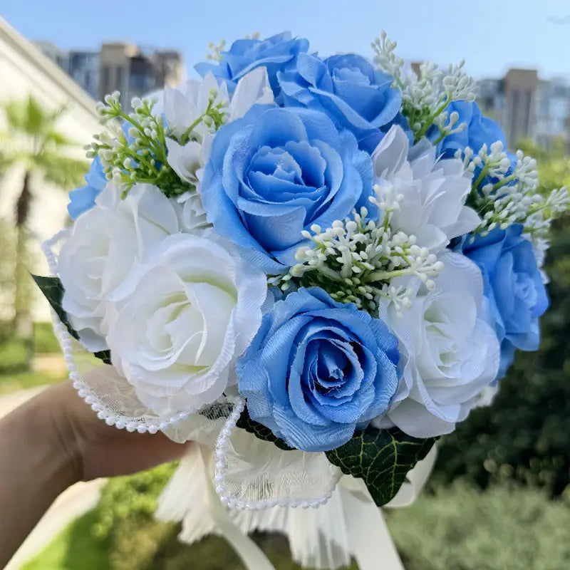 White silk rose wedding bouquet featuring delicate artificial blue and white roses with tiny green filler blooms, tied with a lace ribbon and accented with pearls.