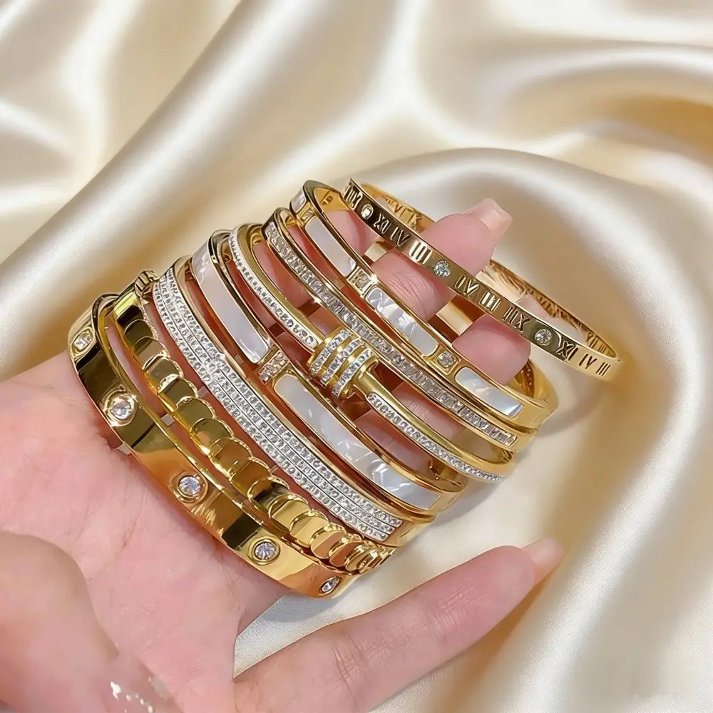 A hand displays stainless steel gold roman numeral bangle bracelets for women featuring intricate designs with sparkling diamonds and mother-of-pearl accents.
