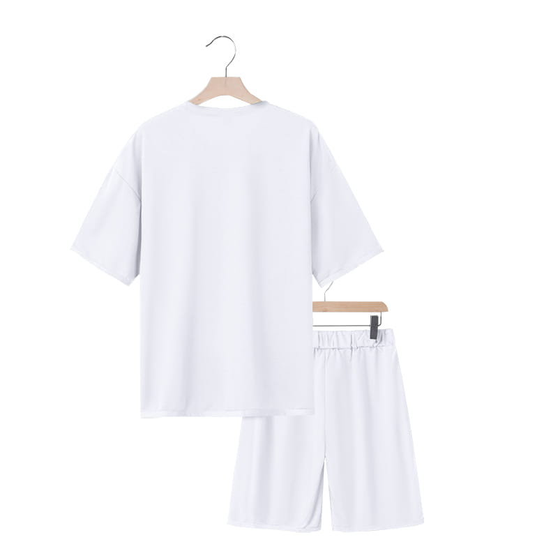 Conjunto veraniego de dos piezas para hombre, que presenta una camiseta casual blanca de algodón y conjunto de pantalones cortos a juego, exhibidos en perchas de madera contra un fondo liso.