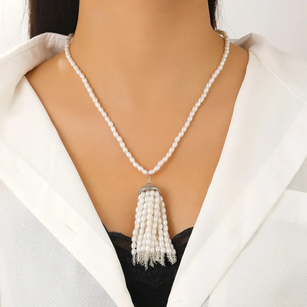 Collier-ras-de-cou élégant en perles blanches avec pendentif à pompon, composé d’une chaîne délicate à perles et d’accents métalliques argentés brillants, conçu comme une longue chaîne de pull-over.