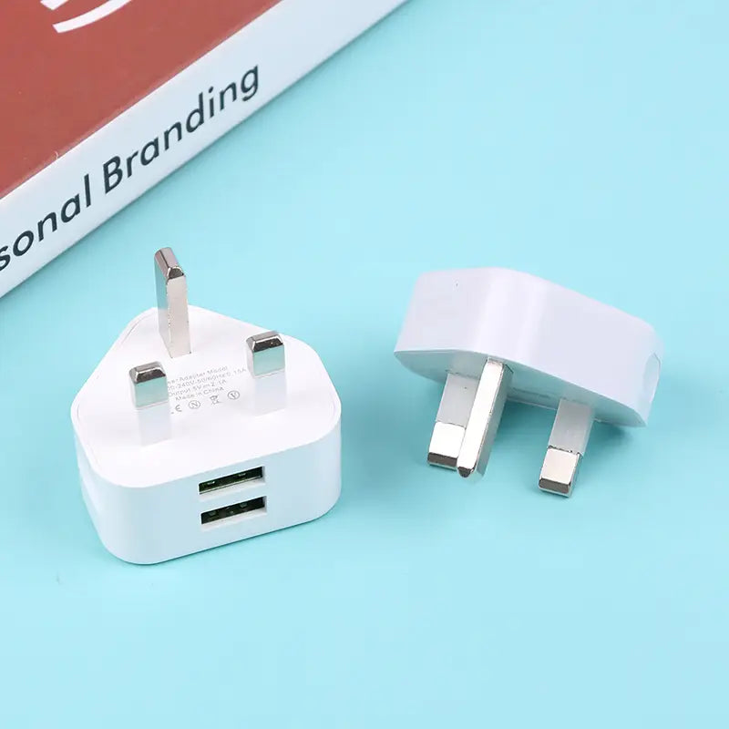 Adaptador de cargador de pared doble USB de 3 clavijas tipo Reino Unido en plástico blanco con dos puertos USB y clavijas metálicas.