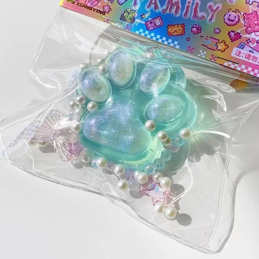 juguete exprimible de pata de gato de silicona translúcido con purpurina color verde azulado, con pequeñas perlas blancas y acentos de cristal rosa, diseñado para aliviar el estrés de forma gradual y lenta.