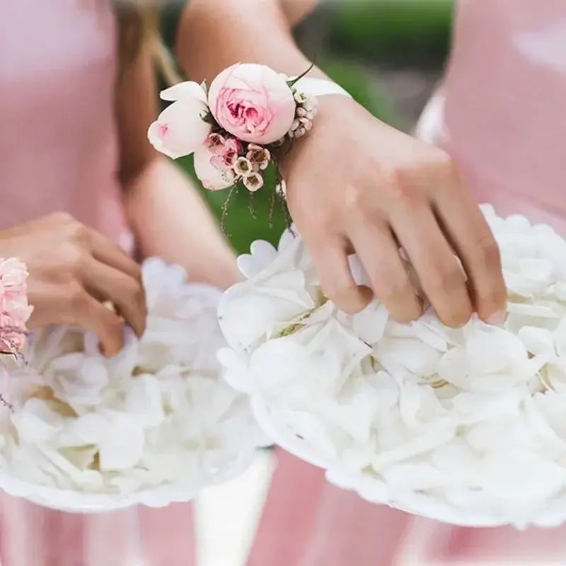 結婚式やパーティーに向けて、小さなつぼみとグリーンをあしらった繊細なピンクと白のフローラルなリストコサージュに、白いシルクのバラの花びらを添えたもの。