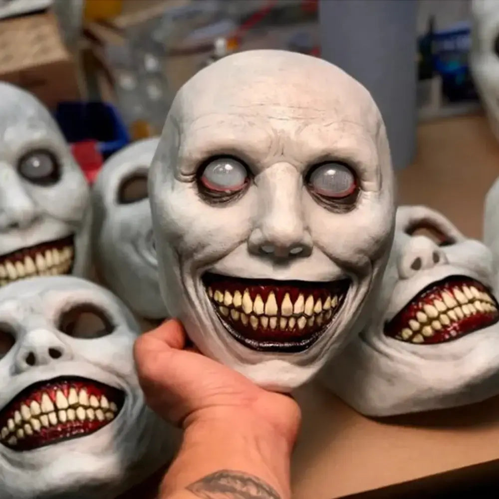 A white latex creepy halloween resin horror mask with exaggeratedly wide eyes and a grotesquely smiling mouth filled with sharp teeth designed as a full face costume accessory.