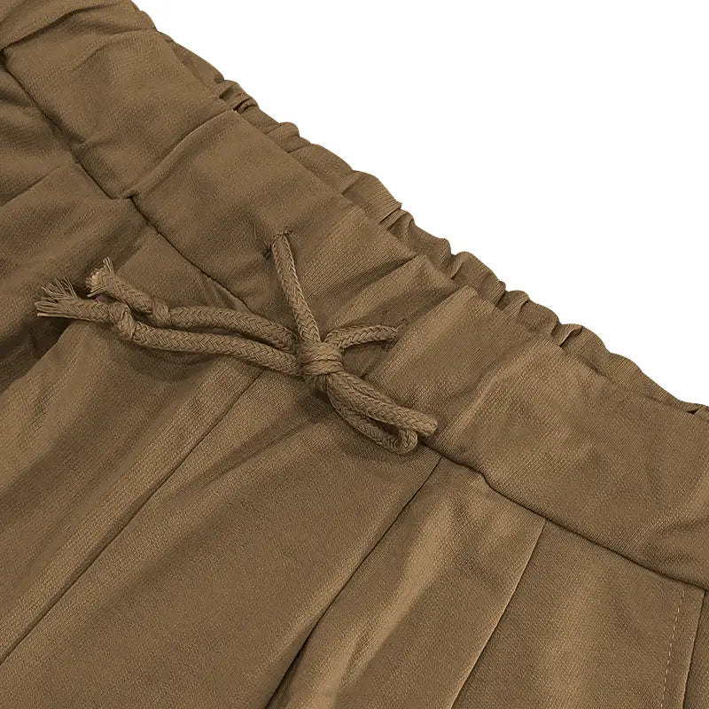 Pantalones beige (tan) plisados con cinturilla con cordón, incluidos en el conjunto veraniego casual para hombre de dos piezas de camiseta y pantalones cortos.