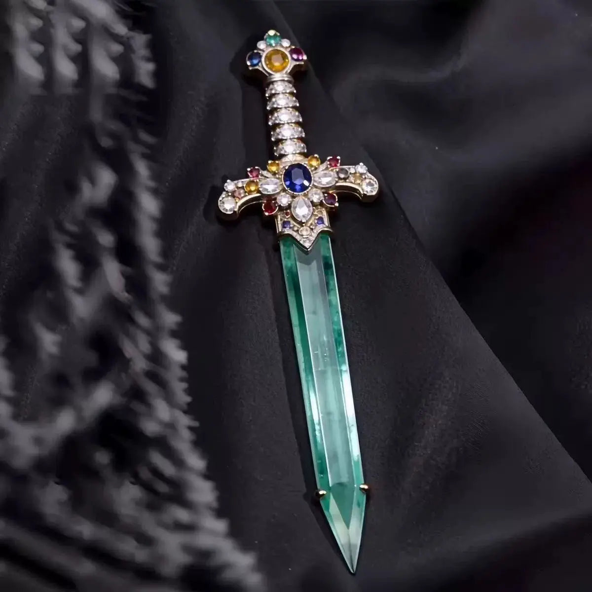Broche en forme d’épée dotée d’une lame de cristal vert translucide et d’une garde ornée, rehaussée de pierres précieuses multicolores.