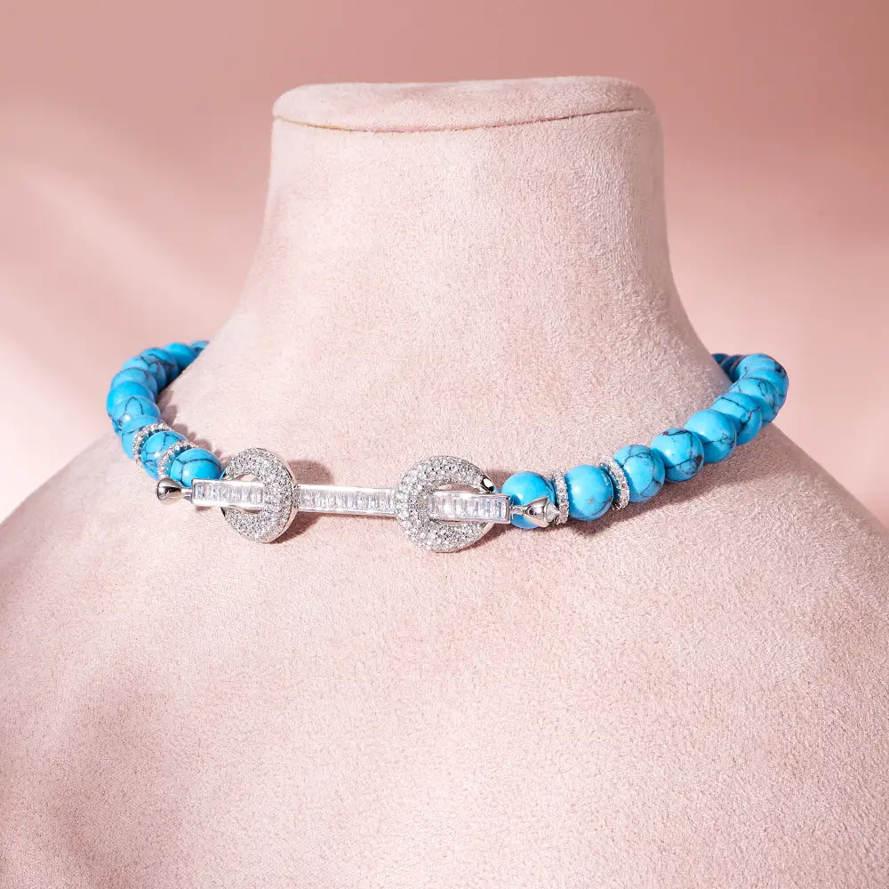 Collar tipo choker con cuentas que presenta cuentas turquesa y un broche engastado de circonita cúbica de tono plateado.