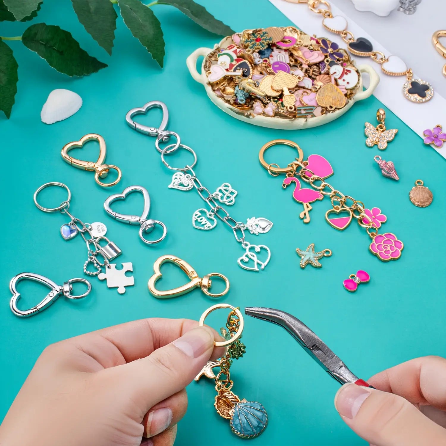 A hand holding a gold-toned enamel heart keychain 3 pack with a heart clasp ring and dangling charms including a seashell and floral designs.