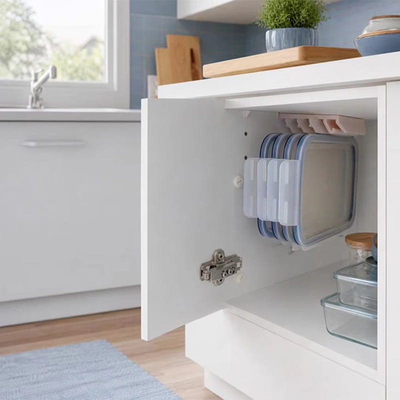 Ensemble de récipients de conservation des aliments en plastique transparent, avec couvercles bleus, rangés avec soin dans un placard blanc à l’aide d’un support de couvercles de récipients de conservation des aliments en plastique et d’une tringle sous étagère.