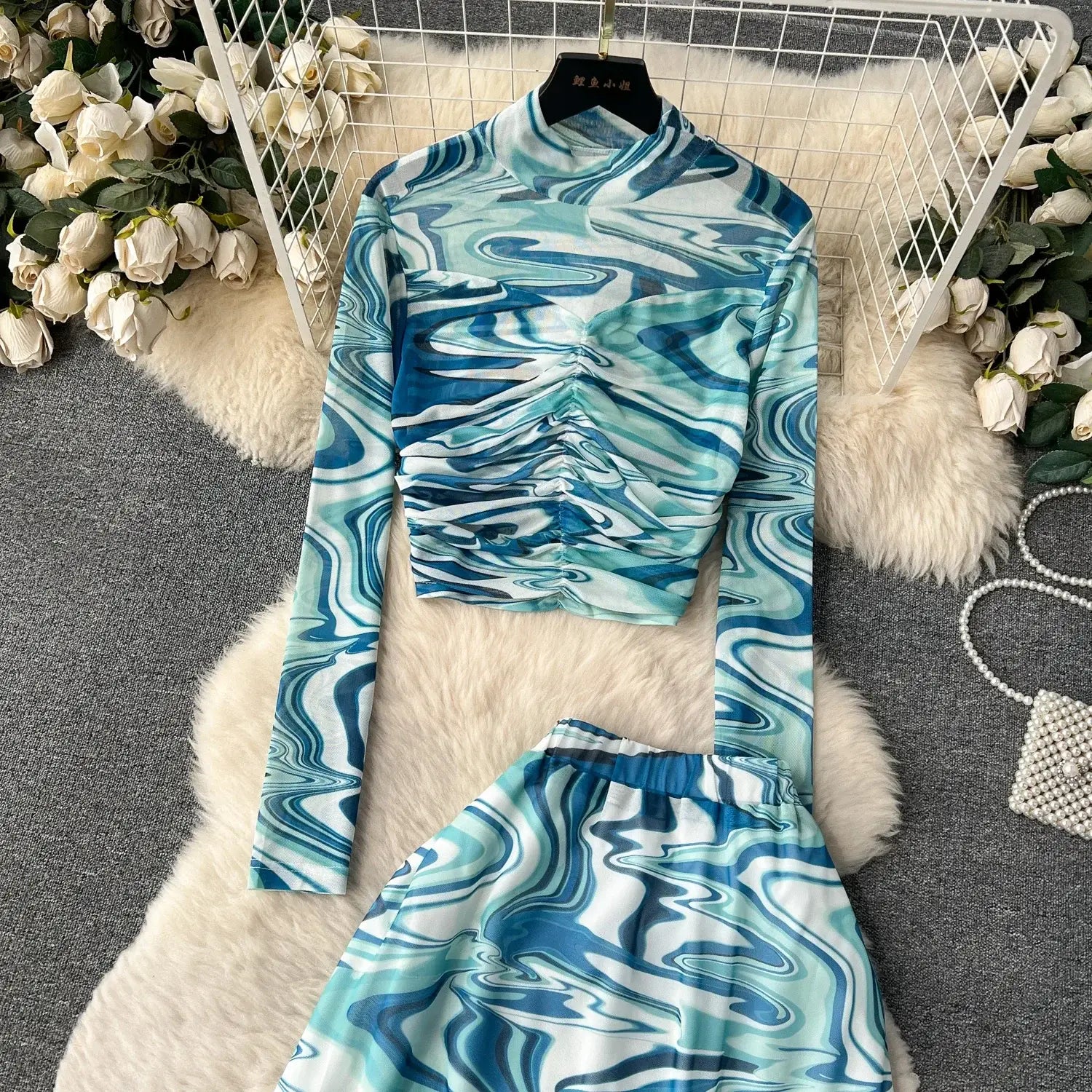 a blue and white marbled long-sleeve crop top with a high neckline and elastic closure displayed on a hanger as part of a two piece mesh skirt set marble print