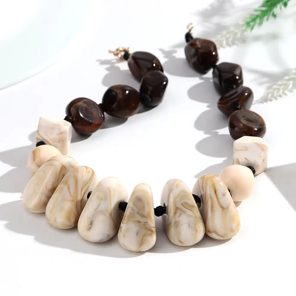 Collier ras du cou en résine à motif géométrique, fait de perles marbrées, présentant une alternance de perles ovales brillantes brun foncé et de perles marbrées en forme de goutte de couleur crème.