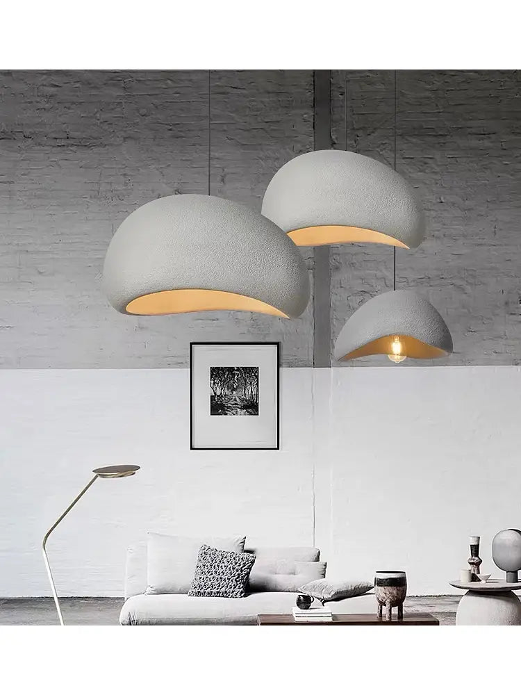 tres luminarias colgantes modernas de hormigón con acabado mate y compartimentos interiores color ámbar cálido, suspendidas en un entorno de sala y comedor