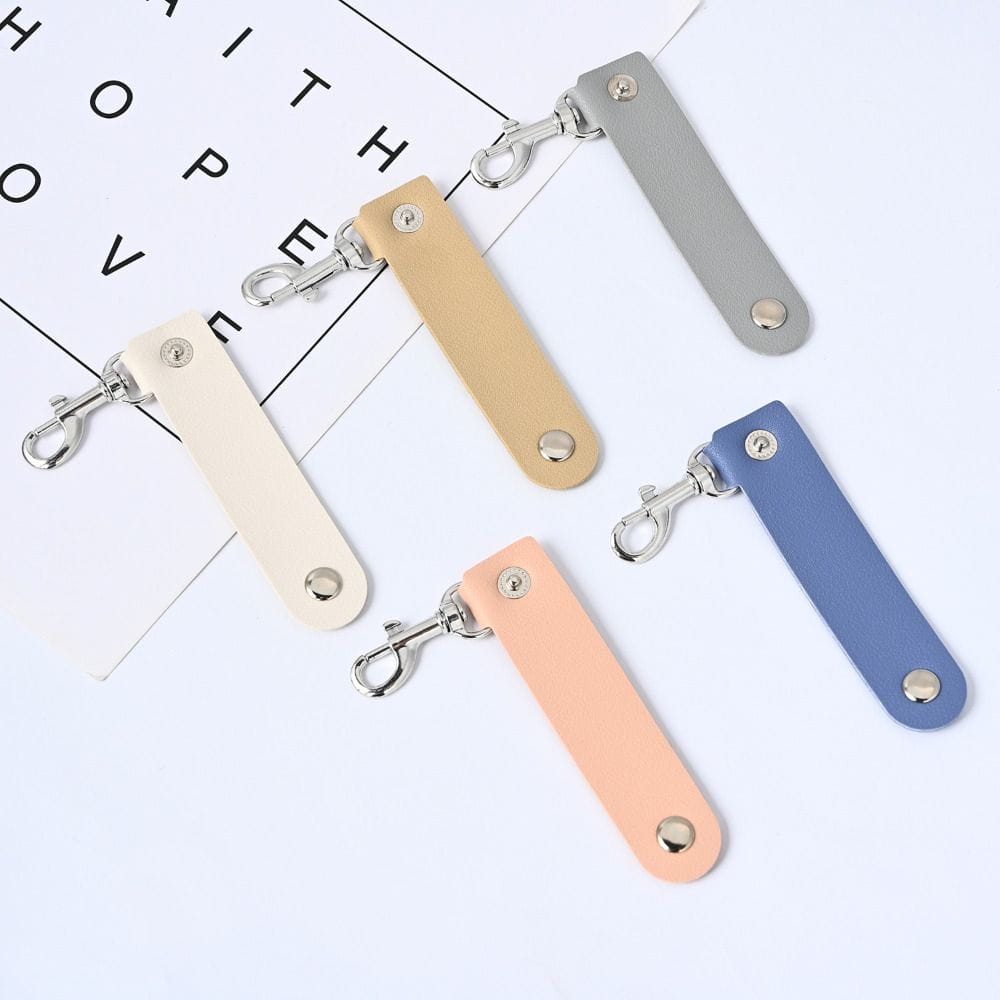 Ein Set aus vier schlanken, rechteckigen Pu-Leder-Schlüsselanhänger-Anhängern mit Anti-Verlust-Autoschlüsselriemen in Beige, Hellbraun, Pfirsich und Blau, jeweils mit einem silberfarbenen Metallverschluss.