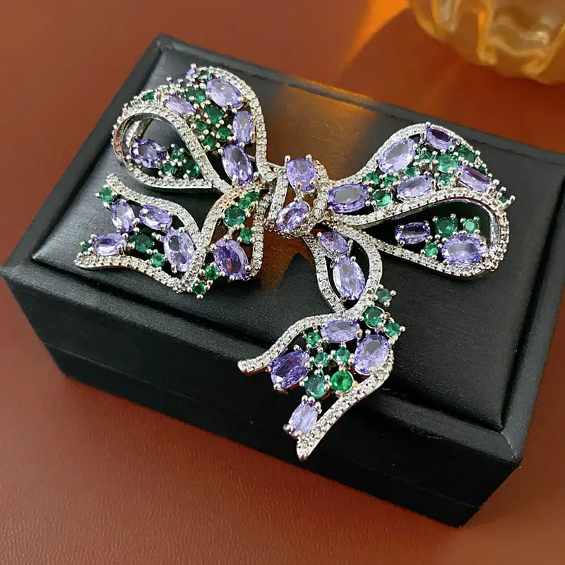 Eine funkelnde silberfarbene Zirkon-Schleifenbrosche mit oval geschliffenen lila- und grünfarbenen Edelsteinen im luxuriösen französischen Schmuckdesign.