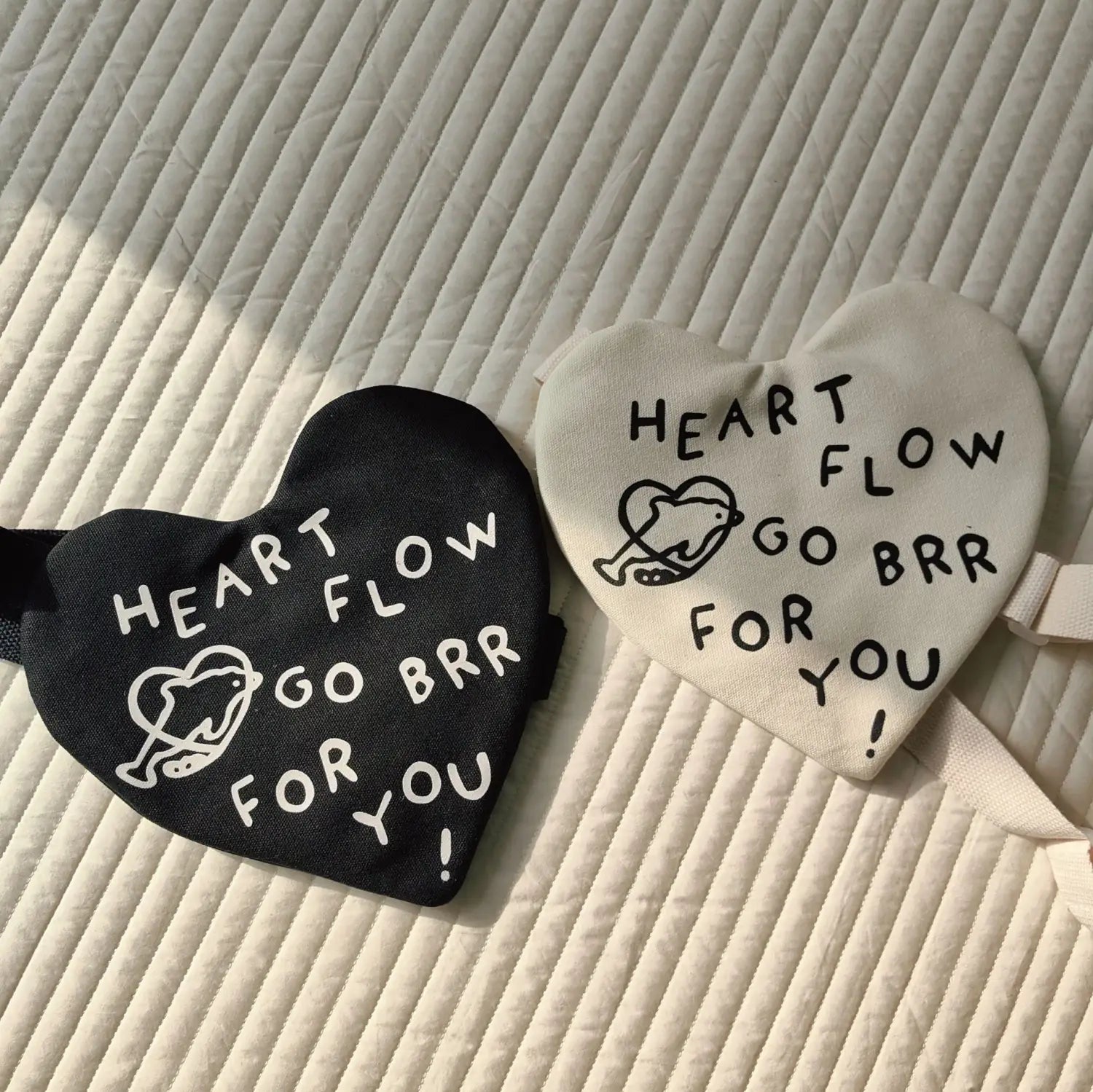 Zwei herzförmige koreanische Kinder-Umhängetaschen mit Herz-Crossbody in Schwarz und Off-White mit weißem Text „heart flow go brr for you“ und einem kleinen illustrierten Herz vorne.