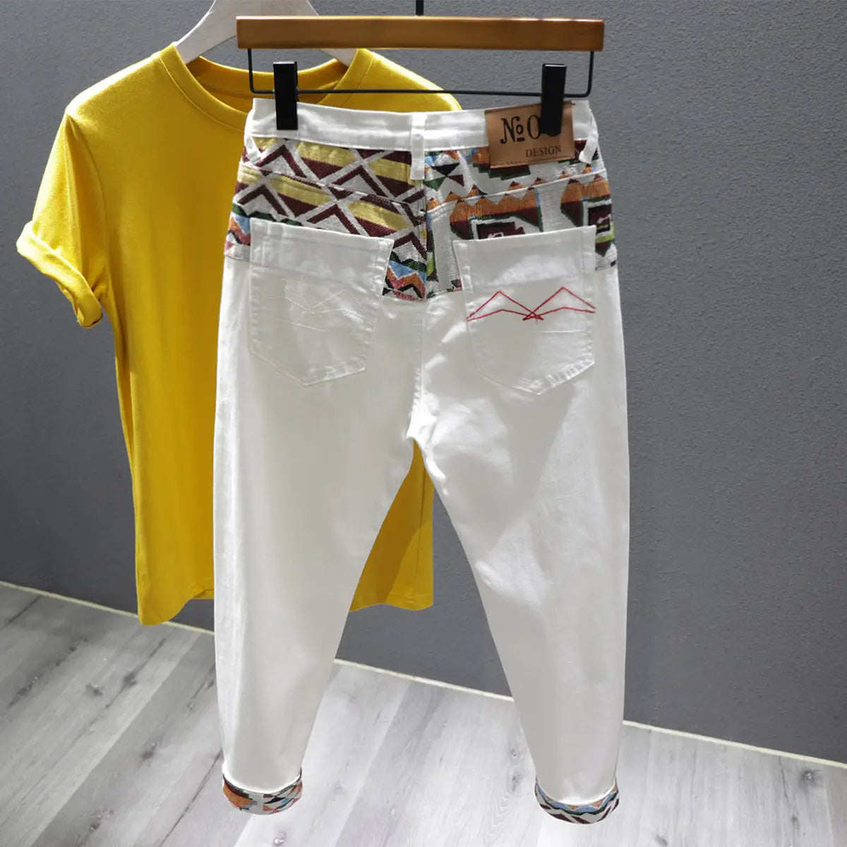 Men slim fit stretch embroidered white denim jeans shown from the back featuring a colorful geometric pattern on the waistband and cuffs with red stitching on the back pocket.