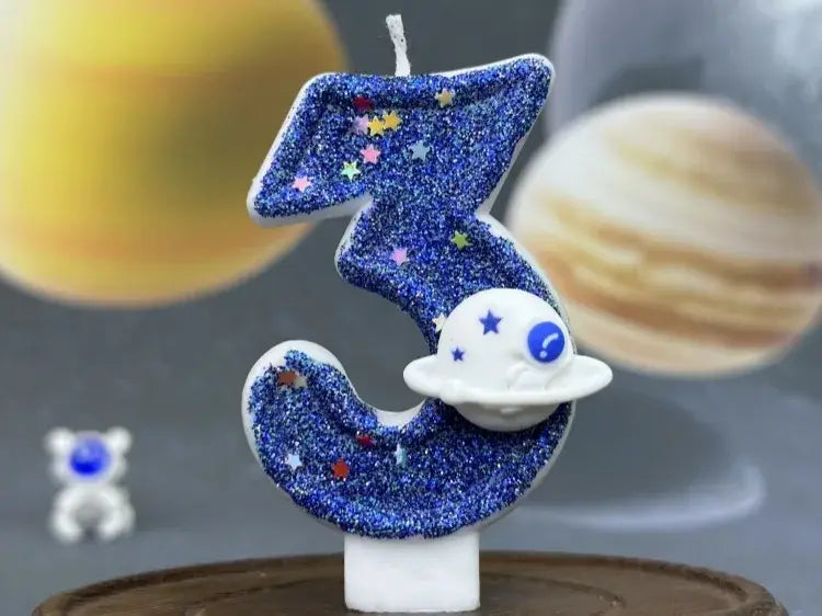 Una vela azul con brillo con el número tres para cumpleaños, con un planeta temático de astronauta blanco y decoraciones de estrellas, utilizada como adorno para pastel de fiesta planetaria.