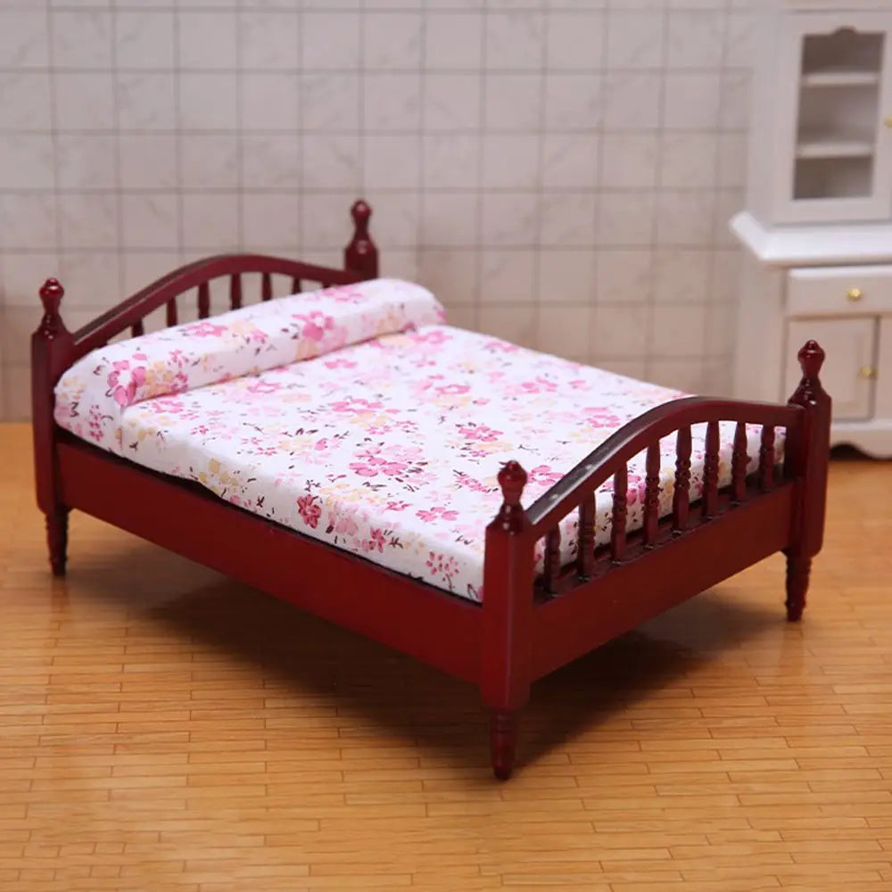 Rotes Holzminiatur-Puppenhaus-Bett mit Matratze und Bettwäsche mit Blumenmuster.