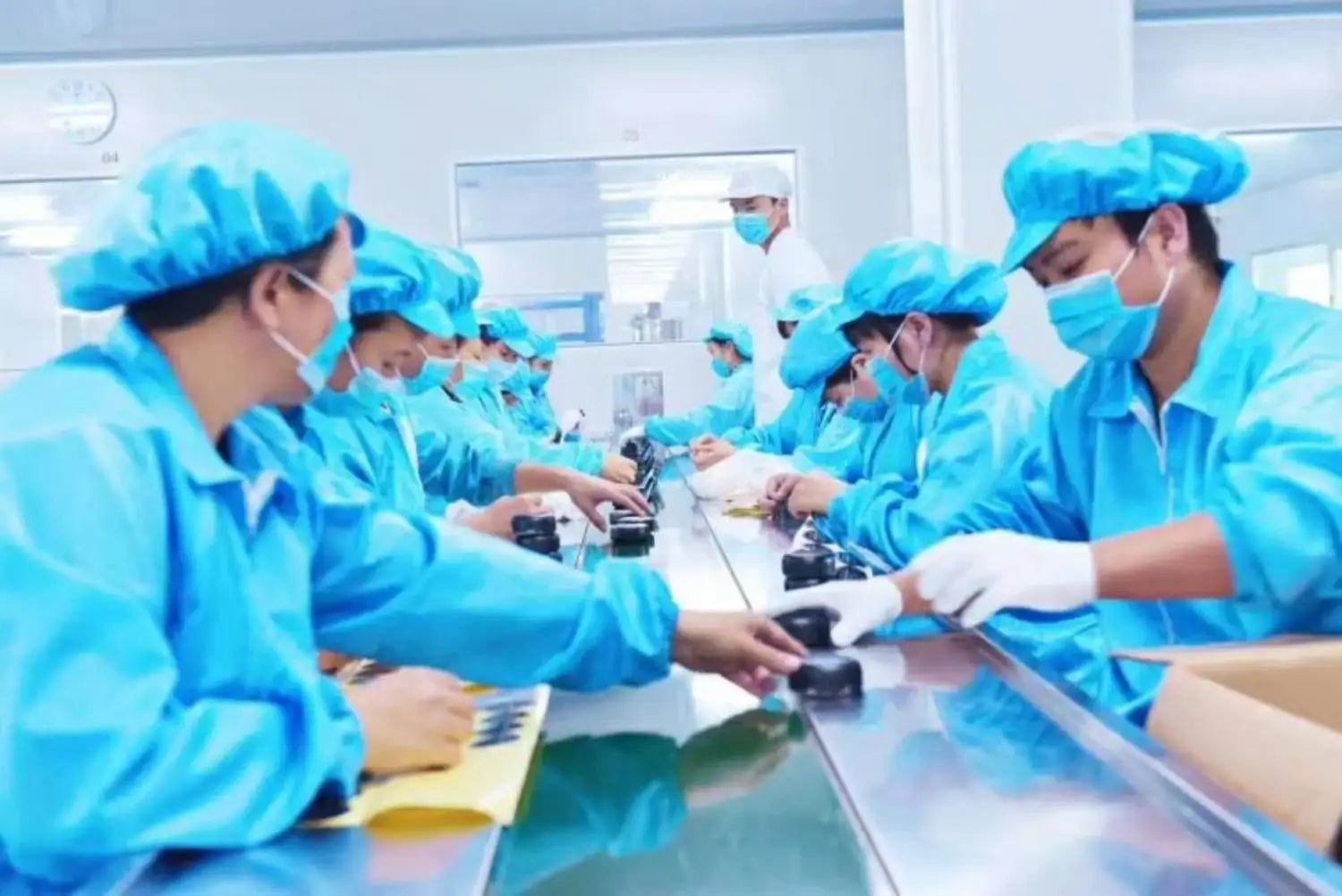 Trabajadores con trajes y gorras de protección azules ensamblando martillos de emergencia negros para automóviles y rompecristales con cortadores del cinturón de seguridad en una cinta transportadora.