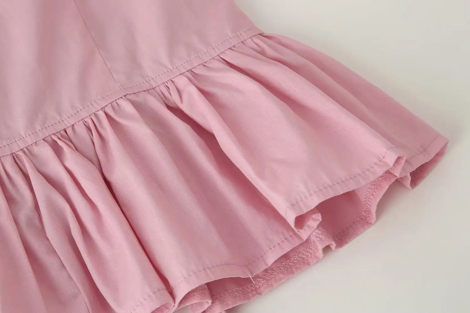 A soft pink women slim fit long sleeve top with a round neckline and delicate stitching featuring a ruffled hem.