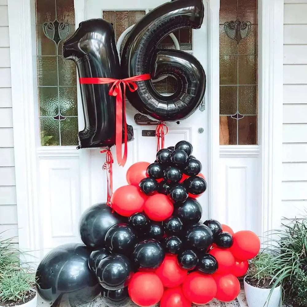 Ein Set aus Rot- und Schwarzem Folienballon, geformt wie die Zahl 16, gebunden mit einem roten Band, für Partydekoration