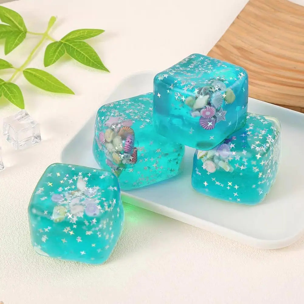 Cube sensoriel à effet anti-stress pour l’océan, avec des glaçons en gel turquoise translucide contenant des coquillages intégrés, des étoiles de mer et des étoiles scintillantes, constituant un cadeau attentionné.