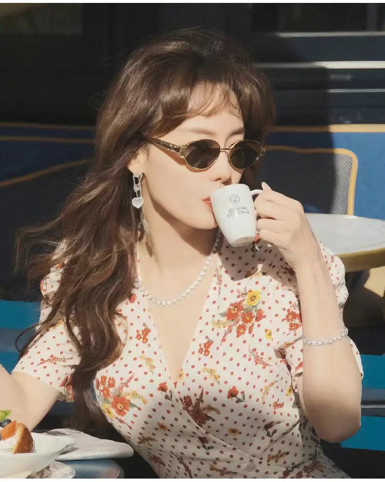 Taza de café de cerámica blanca con un diseño floral sutil, mostrada junto con gafas de sol ovaladas con montura dorada para mujer y hombre.