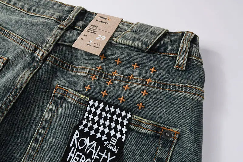 men’s distressed blue acid wash denim shorts featuring dark-wash denim with a distinctive white houndstooth patch and black text reading royalty heroes accented by orange cross-shaped stitching on the back.