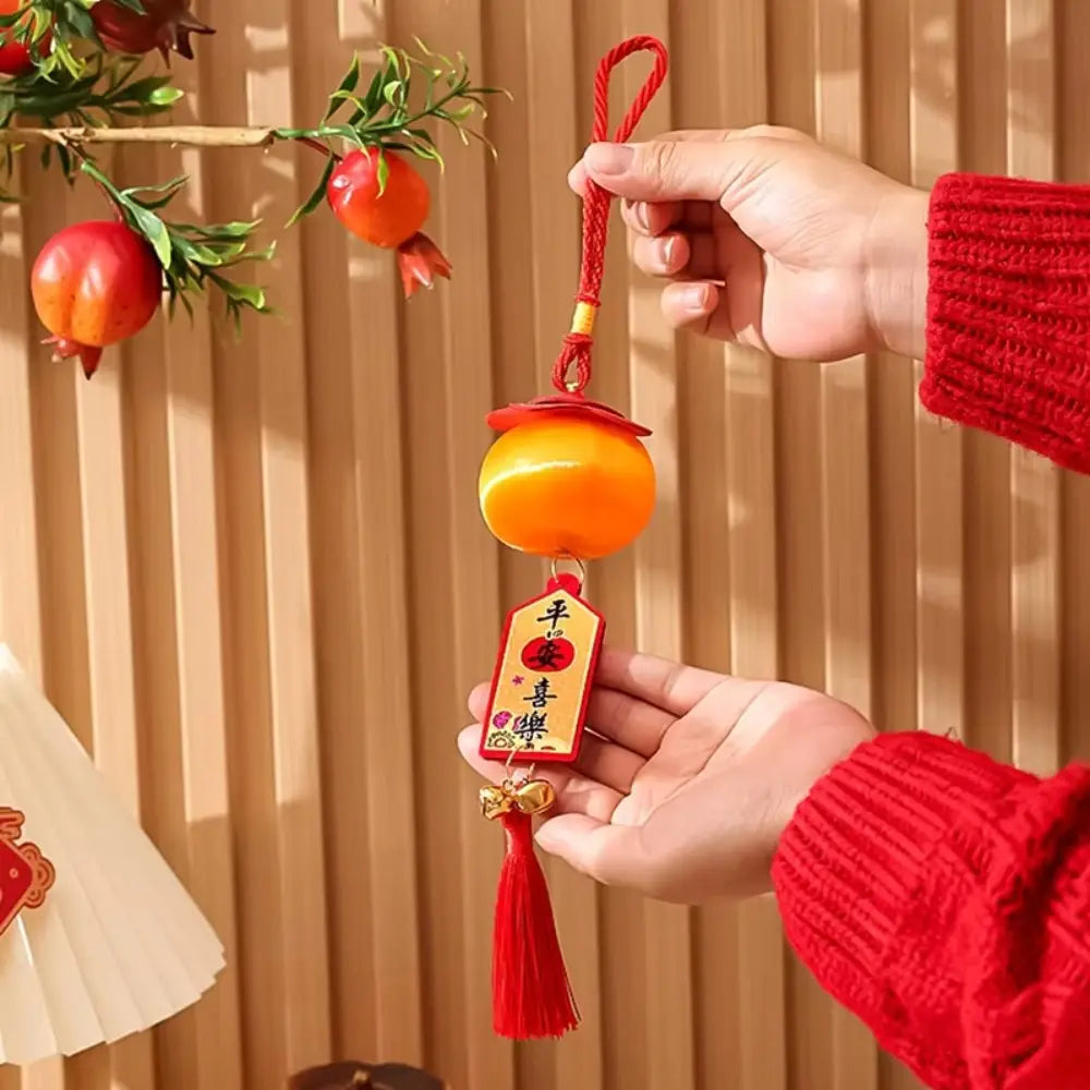 Ein leuchtend roter und orangefarbener Laternenanhänger zum Chinesischen Neujahr 2025 mit Quasten: mit einem glänzenden Anhänger in Pflaumen-/Granatapfelform sowie einem rechteckigen Anhängeetikett mit glückverheißenden Zeichen.