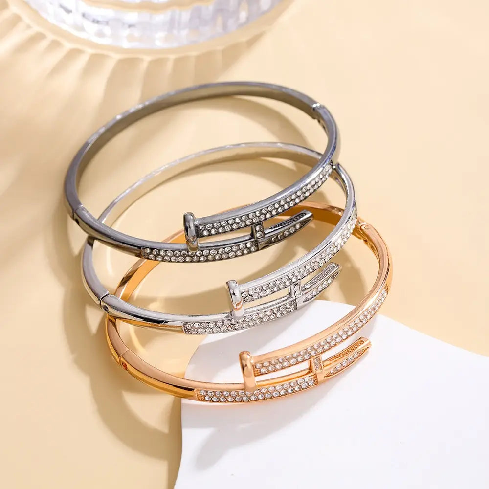Trois bracelets jonc intersectants en zirconium cubique élégants, finition argent et or rose, chacun orné d’une rangée de cristaux transparents étincelants le long de la monture.