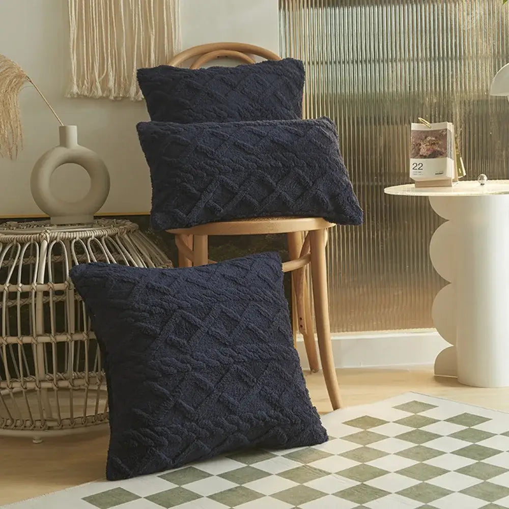 Drei navyblaue Kissenbezüge mit strukturiertem Diamantmuster-Strickstoff im Format 45x45 cm, auf und um einen Holzhocker herum angeordnet zur dekorativen Verwendung.