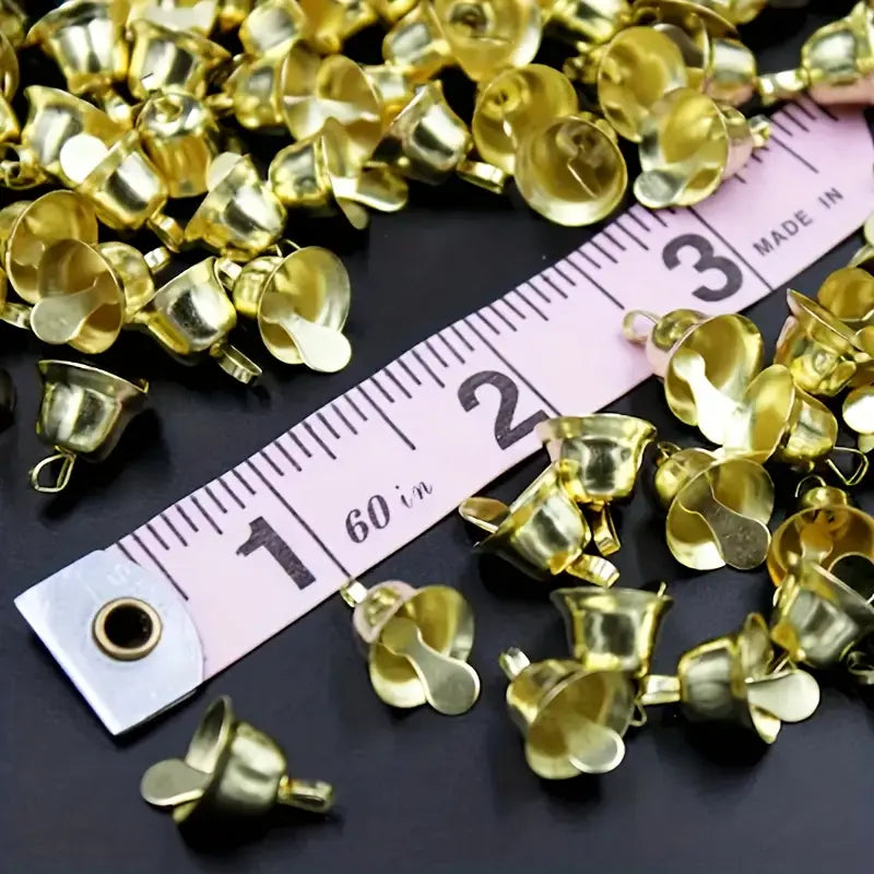 Des clochettes de traîneau en métal doré, 20 pièces, avec de petites breloques dorées en forme de cloche disposées autour d’un mètre ruban.