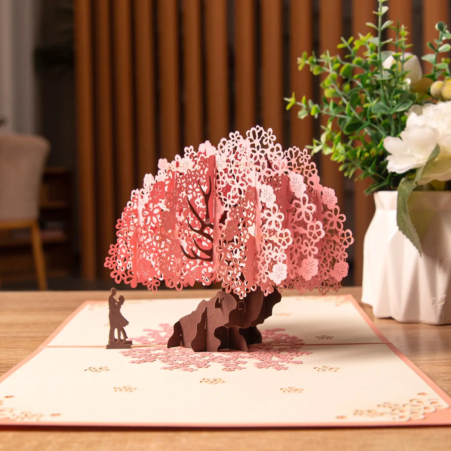 Carte de la Saint-Valentin 3D à effet pop-up rose délicate en fleurs de cerisier, présentant des pétales découpés avec finesse et une silhouette romantique d’un couple sous l’arbre.