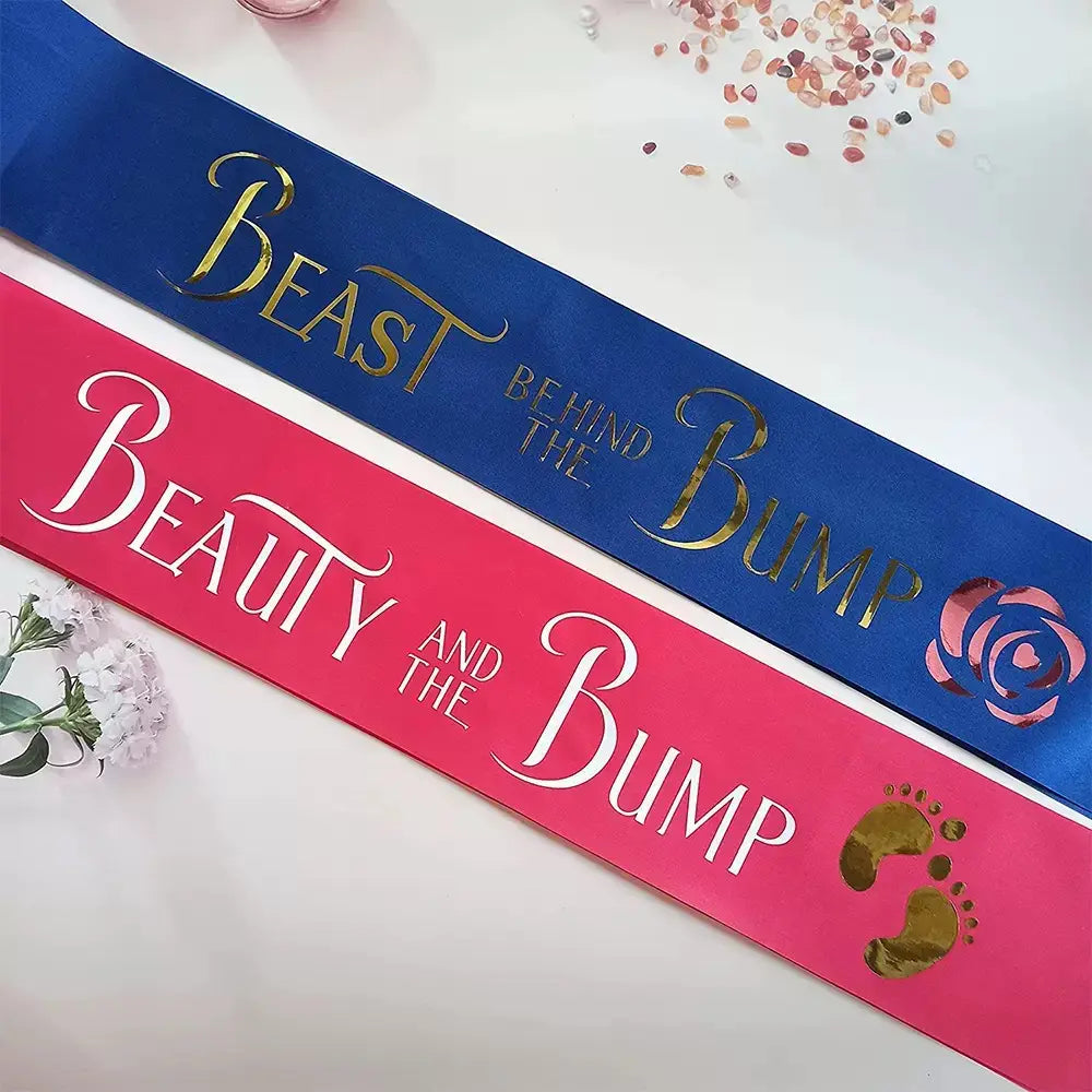 Ensemble d’écharpe de douche bébé comportant une écharpe en satin fuchsia et bleu royal, avec une inscription en lettres dorées indiquant « beauty and the bump » et « beast behind the bump », ornée d’un motif de rose et d’empreinte.
