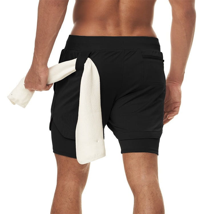 Men 2 in 1 gym shorts in black quick dry fabric with layered design and side pockets shown from the back with a white towel draped over them.