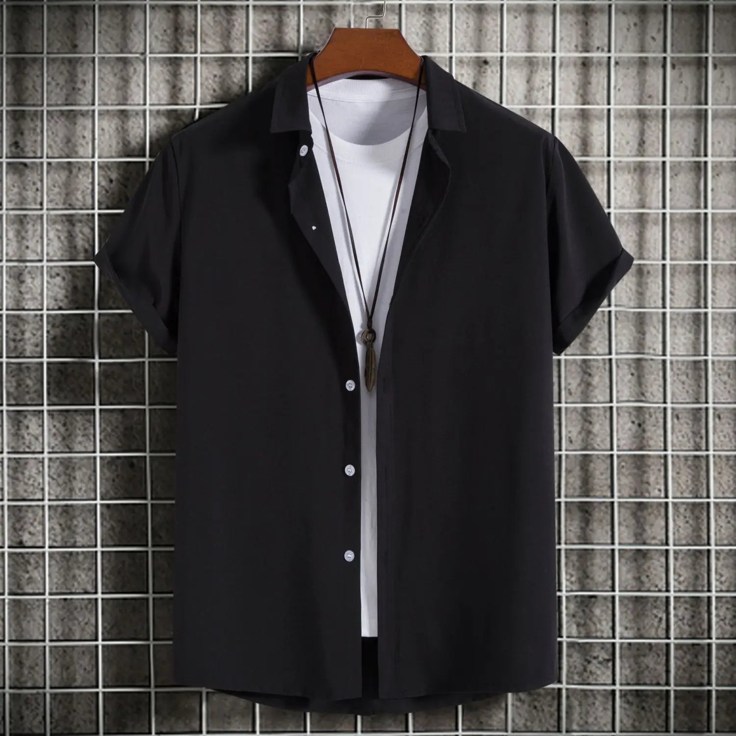 Chemise noire à manches courtes pour homme, avec boutons et col, affichée sur un cintre en bois contre un fond quadrillé, idéale pour des chemises de plage décontractées et des looks unis pour hommes.