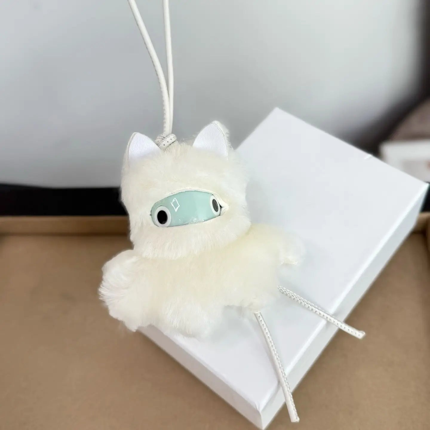 Un llavero colgante para bolso con encanto de animales de cuero esponjoso color blanco, con rostro verde menta, ojos negros, orejas pequeñas blancas y patas colgantes, diseñado como un tierno llavero de gato tipo peluche.